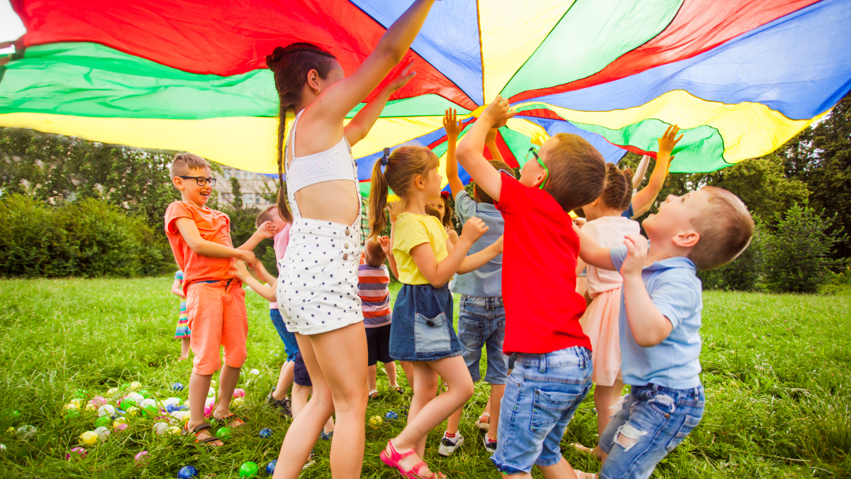 Imagen de una manotora y un grupo de niños jugando debajo de una bandera de colores